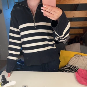 Randig svartvit stickad tröja half zip - Säljer en svart och vit randig stickad tröja med half zip-dragkedja i halsen. Tröjan har långa ärmar och breda ribbade muddar. Perfekt för dig som gillar en chill och stilren look med lite marint vibe.