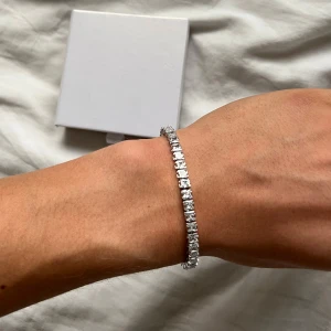 Tennisarmband i silver - Snyggt tennisarmband i silverfärg med gnistrande Swarovski liknande fyrkantiga stenar längs hela bandet. Armbandet har en klassisk och stilren design som verkligen poppar och ger en lyxig känsla. Perfekt accessoar för att lyfta din outfit med extra bling.