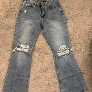 Ljusblå ripped jeans med raka ben - Säljer ett par ljusblå jeans med raka ben och slitna detaljer på båda knäna. Klassisk femficksmodell med hög midja och snyggt tvättad denim. Perfekta för en avslappnad och trendig look.