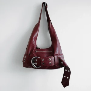 Väska 🥰 - Trendig axelväska i en vacker djup burgundy färg! ⛓️🥰Mått: 38x20x8cm, remmen är 38cm från mittersta hålet men kan justeras kortare eller längre 📏Tyvärr aldrig fått användning för den så som ny! ✨OBS färgen är lite svårfångad på bild men är mest lik sista bilden. Köp nu 💌