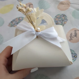 Väska - Supergullig liten kuvertväska i vit syntet med handtag, dekorerad med en vit rosett, pärldetalj och torkade blommor. Perfekt accessoar för att lyfta din outfit med en romantisk touch.