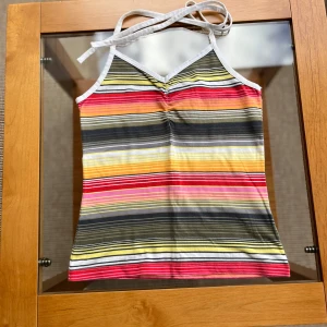 Randigt linne från Marwin - Radigt linne från Marwin i storlek XS. Toppen har smala axelband som knyts i nacken och är perfekt för varma dagar. Mönstret har ränder i rosa, rött, gult, grönt och vitt.