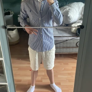 Blåvit randig skjorta från Polo Ralph Lauren - Klassisk blåvit randig skjorta från Polo Ralph Lauren med button-down krage och broderad logga på bröstet. Skjortan har långa ärmar och knäppning framtill. Perfekt för en stilren och tidlös look. Säljer den på grund av att den inte passar mig på längden