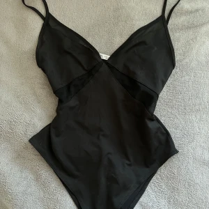 Svart body med mesh från Zara - Svart body från Zara med tunna axelband och snygga meshdetaljer vid bysten och sidorna. V-ringad framtill och figurnära passform som ger en clean och stilren look. Mer som storlek Xs! Aldrig använd bara testad