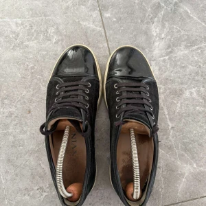 Svarta sneakers från Lanvin i mocka och skinn - Snygga svarta sneakers från Lanvin med ovandel i mocka och lackad skinn-tå. Skorna har svarta snören, rund tå och vit sula. Perfekta för dig som gillar stilrena och exklusiva sneakers med en lyxig touch. Dm för frågor 🤝