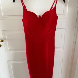 Röd tight långklänning med bygel - Snygg röd långklänning med figurnära passform och bygel vid bysten. Klänningen har smala axelband och en markerad urringning. Perfekt för dig som vill sticka ut med en klassisk och stilren look.