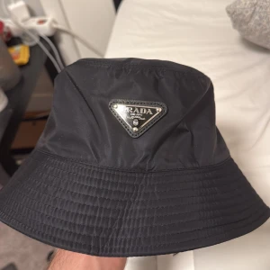 Svart bucket hat från Prada - Säljer denna bucket hat eftersom att jag inte kommer använda den. Helt ny oanvänd. Pris kan diskuteras vid snabb affär! 