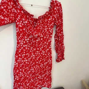 Röd blommig klänning från Parisian - Röd kortklänning från Parisian med vita blommor, långärmad. Klänningen har en v-ringning och figurnära passform. Jättefin men för liten kan skicka bild på om de behövs.