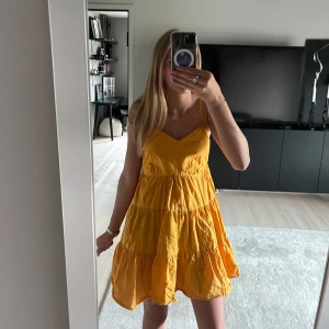 Kortklänning med volanger - Superfin orange kortklänning med tunna axelband och volanger i flera lager. Klänningen har en v-ringad urringning framtill. Hör av dig om du har några frågor eller funderingar!🩷