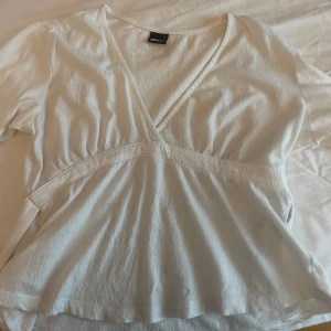 Vit omlottblus från Gina Tricot - Supersöt vit omlottblus från Gina Tricot med v-ringning och långärmade armar. Det finns även två band ifall man vill knyta en rosett i ryggen💞
