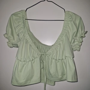 Ljusgrön croppad blus med knyt - Superfin ljusgrön blus med kort ärm och croppad passform. Djup v-ringning och volangdetaljer, samt knyt framtill. Köpt på Vinted. I väldigt fint skick. Storlek M men lite liten i storleken ( har vanligtvis S-M och C kupa ) Katt finns i hemmet. 