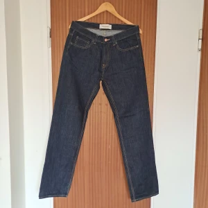 Mörkblå jeans från Dressmann - Klassiska mörkblå jeans från Dressmann med raka ben och kontrastsömmar. Jeansen har fem fickor och stängs med knapp och dragkedja. Perfekta för dig som gillar en enkel och tidlös stil.