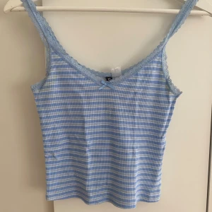 Blå- och vitrandig linnetopp från HM divided  - Supersöt blå och vitrandig linnetopp från HM Divided med spetskant och liten rosett framtill. Tunt och mjukt material, smala axelband och v-ringad hals. Perfekt för varma dagar eller som layering-piece. Säljer i storlek S!