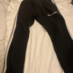 Palm Angels svarta mjukisbyxor med ränder - Svarta mjukisbyxor från Palm Angels med vita sidoränder och logga broderad på låret. Skriv för mer bilder 