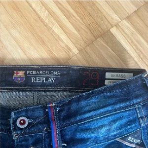 Replay Anbass FC Barcelona jeans - Snygga mörkblå Replay Anbass jeans i samarbete med FC Barcelona. Klassisk femficksmodell med röda och blå detaljer vid knapp och fickor. Jeansen har en slim passform och är tillverkade i stretchig denim för extra komfort.