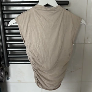 Beige ärmlös croppad topp - Snygg beige topp med ärmlös design och croppad passform. Från Gina tricot