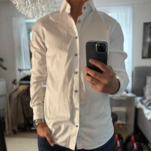 Vit skjorta Stenströms slimline - Vit skjorta från Stenströms i slimline-modell med blå knappar och snyggt blommigt mönster på insidan av krage och manschetter. Tillverkad i tvåfaldig super cotton som känns lyxig och skön. Perfekt för dig som gillar stilrena detaljer och en smal passform.