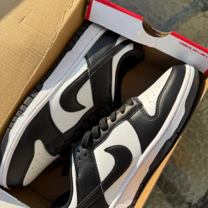 Nike Dunk Low Retro svart/vit EUR 44 - Nike Dunk Low Retro i klassisk svart och vit färg. Skorna har svart läderöverdrag, vit bas och svarta snören, med extra vita skosnören. Snygg låg siluett och ikonisk Swoosh-logga på sidorna. Perfekta för dig som gillar streetwear och tidlös stil.