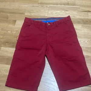 Röda shorts från Pitbull, W30 - Snygga röda shorts från Pitbull i klassisk modell med fickor fram och bak. Tillverkade i mjuk bomull med lite stretch för extra komfort. Perfekta för sommardagar och har en stilren look som funkar till det mesta.