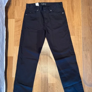 Svarta Jay Satin Jeans 31/34 - Svarta jeans från J.Lindeberg i modellen Jay Satin Jeans. Byxorna har en klassisk femficksdesign, raka ben och är tillverkade i ett mjukt satinliknande material som ger en snygg finish. Perfekta för dig som gillar stilrena och moderna byxor.