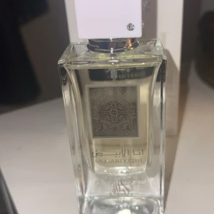  Lattafa Ana Abiyedh parfym 60ml - Ana Abiyedh från Lattafa är en elegant parfym i en genomskinlig glasflaska med vit fyrkantig kork och silverdetaljer. Doften kommer i en stilren vit förpackning med silvertext och arabiska inslag. Perfekt för dig som gillar unika och fräscha dofter.