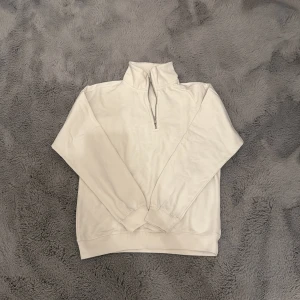 Vit half zip sweatshirt - Snygg vit sweatshirt med half zip och hög krage. Tröjan har lång ärm och är tillverkad i mjuk bomull, perfekt för lager-på-lager. Enkel och stilren design som passar till allt.