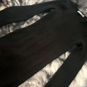 Svart långärmad klänning 157 XS - Svart söt långärmad klänning från 157 i storlek XS. Klänningen är ribbad och har en lätt vågig kant nertill. Materialet är stretchigt och strukturerat, vilket ger en cool och modern känsla.