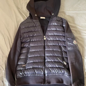 Mörkblå moncler cardigan - Snygg mörkblå cardigan från Moncler. Jackan har huva, dragkedja framtill och två dragkedjefickor. Perfekt för sommar kvällarna nu men också tills hösten, passar rätt så bra året runt. Denna tvättas såklart innan jag fraktar samt att priset kan diskuteras