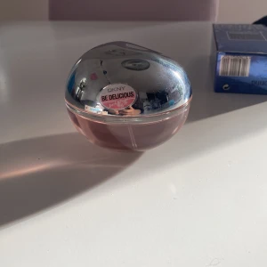 DKNY Be Delicious Fresh Blossom parfym - Säljer en DKNY Be Delicious Fresh Blossom parfym med rund, äppelformad flaska i glas och silverfärgat lock. Parfymen har en ljusrosa ton och en fräsch, blommig doft. Perfekt för dig som gillar feminina och fruktiga dofter.