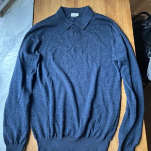 Blå merinoull pikétröja John Henric - Snygg marinblå pikétröja från John Henric i 100% merinoull. Tröjan har klassisk krage, tre knappar framtill och långa ärmar. Perfekt för dig som gillar stilrena och bekväma plagg med premiumkänsla.