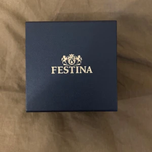 Festina herrklocka i silver med blå urtavla - Stilren Festina herrklocka med länkarmband i silverfärgat stål och mörkblå urtavla. Klockan har dag- och datumvisning samt klassisk design med tydliga index. Levereras i originalask och extra länkar medföljer.