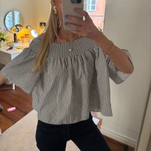 Randig offshoulder blus - Säljer en luftig och croppad blus med svarta och vita ränder. Blusen har offshoulder-modell och vida, korta ärmar. Perfekt för varma dagar och ger en trendig look.