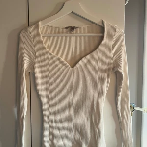Vit tröja - Säljer en vit ribbad långärmad topp från H&M med snygg v-ringning. Toppen är figurnära och har en mjuk, stretchig känsla som passar perfekt till jeans eller kjol. Använda fåtal gånger.