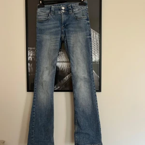 Blå bootcut jeans med lågmidja  - Snygga blå bootcut jeans med lågmidja och lätt slitning och tvättade detaljer. Klassisk femficksmodell med dubbla knappar i midjan och fickor med lock bak. Jeansen har en något utsvängd passform nertill och är perfekta för en avslappnad men trendig look.