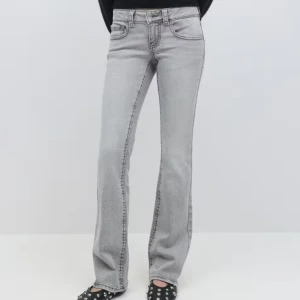 Grå bootcut jeans med fickdetaljer - Snygga grå jeans med bootcut-modell och markerade sömmar. Byxorna har klassiska fem fickor och bakfickor med lock och knapp. Perfekta för dig som gillar en retrovibe och vill ha ett par jeans som sticker ut lite extra.