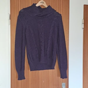 Lila stickad tröja från Mexx - Säljer en lila stickad tröja från Mexx med snygg kabelstickad detalj framtill och hög krage. Tröjan har långärmade ärmar och ribbade muddar för extra komfort. Perfekt för dig som gillar en mysig och stilren look.