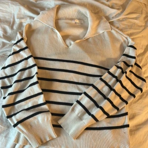 Randig stickad tröja från Gina Tricot - Snygg stickad tröja från Gina Tricot i vitt med svarta ränder. Tröjan har v- ringad krage