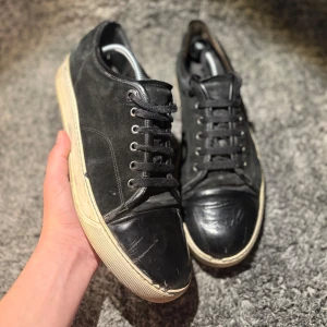 Lanvin skor  - Svarta sneakers med ovandel i mocka och tåparti i skinn. Skorna har svarta snören, silverfärgade öljetter och en beige platt sula. Klassisk rund tå och stilren design som passar till det mesta.