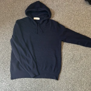 Mörkblå hoodie i kashmir ifrån Sayless - Mysig mörkblå hoodie från Sayless. Tröjan har huva med snörning och långa ärmar. Perfekt för dig som gillar en stilren och enkel look med premiumkänsla. Passformen är normal och materialet är supermjukt.