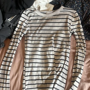 Randig långärmad tröja Gina Tricot - Superskön långärmad tröja från Gina Tricot i vitt med svarta horisontella ränder. Modellen är tight och har rund halsringning. Perfekt basic-plagg att styla med jeans eller kjol. Materialet är mjukt och stretchigt, troligtvis bomullsmix.