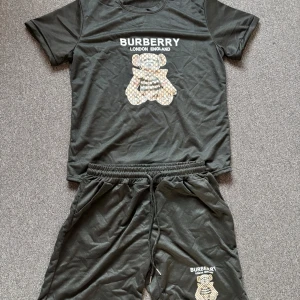 Svarta Burberry set - Svarta shorts från Burberry med elastisk midja och snörning. På vänster ben finns ett tryck med Burberry-logga och en nalle i beige och svart mönster. Mjukt bomullsmaterial som är skönt. 