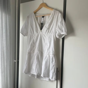 Vit klänning med v-ringning - Säljer en söt vit klänning med v-ringning och korta ärmar. Klänningen har en volangdetalj nedtill och är perfekt för sommardagar. Den är tillverkad i ett lätt och luftigt material.