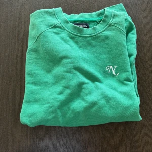 Grön tröja från New Black - Säljer en snygg grön tröja från New Black med ett stilrent broderat 'N' på bröstet. Färgen är väldigt stilren 