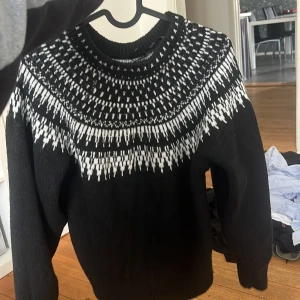 Svart stickad tröja med mönster - Säljer en svart stickad tröja med ett snyggt vitt mönster runt halsen. Tröjan har långa ärmar och en rund halsringning!
