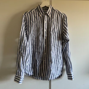 Randig skjorta från John Henric - Säljer en stilren randig skjorta från John Henric i blått och vitt. Skjortan har långa ärmar och knappar framtill. Perfekt för en klassisk look med en modern touch. Den är lite nopprig men tror den ska va så. Om man kollar på sista bilden så ser man hur den ser ut på deras hemsida. Annars bra skick på den. Nypris 999kr