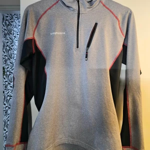 Grå och svart tröja från Bagheera - Säljer en grå och svart tröja från Bagheera med röda sömmar och en praktisk dragkedja framtill. Perfekt för kyliga dagar med sin långa ärmar och bekväma passform. Tröjan har även en liten bröstficka med dragkedja.