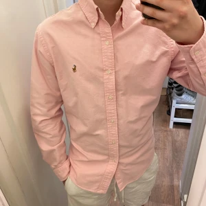  Polo Ralph Lauren (Rosa skjorta) - Säljer en stilren rosa skjorta från Polo Ralph Lauren. Skjortan. Perfekt för en snygg och avslappnad look. Den är oanvänd och redo för en ny ägare! Den är storlek L!