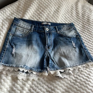Jeansshorts med spetsdetalj från Place du Jour - Snygga jeansshorts i blå denim från Place du Jour med coola slitningar och unik spetsdetalj längs fållen. 