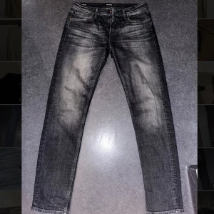 Svarta jeans från Jack & Jones - Snygga svarta jeans från Jack & Jones med en klassisk femficksdesign. De har en lätt tvättad look och raka ben. Perfekta för en stilren vardagslook. Storlek W33 L36