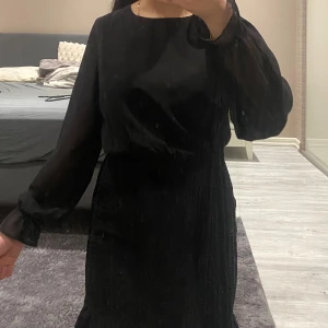 Svart klänning med långa ärmar - STORLEKEN ÄR 158 MEN PASSAR XXS ‼️‼️Elegant svart klänning med långa ärmar och smockdetaljer i midjan. Perfekt för en stilren look. Materialet ger en fin passform och klänningen har en klassisk rund halsringning.